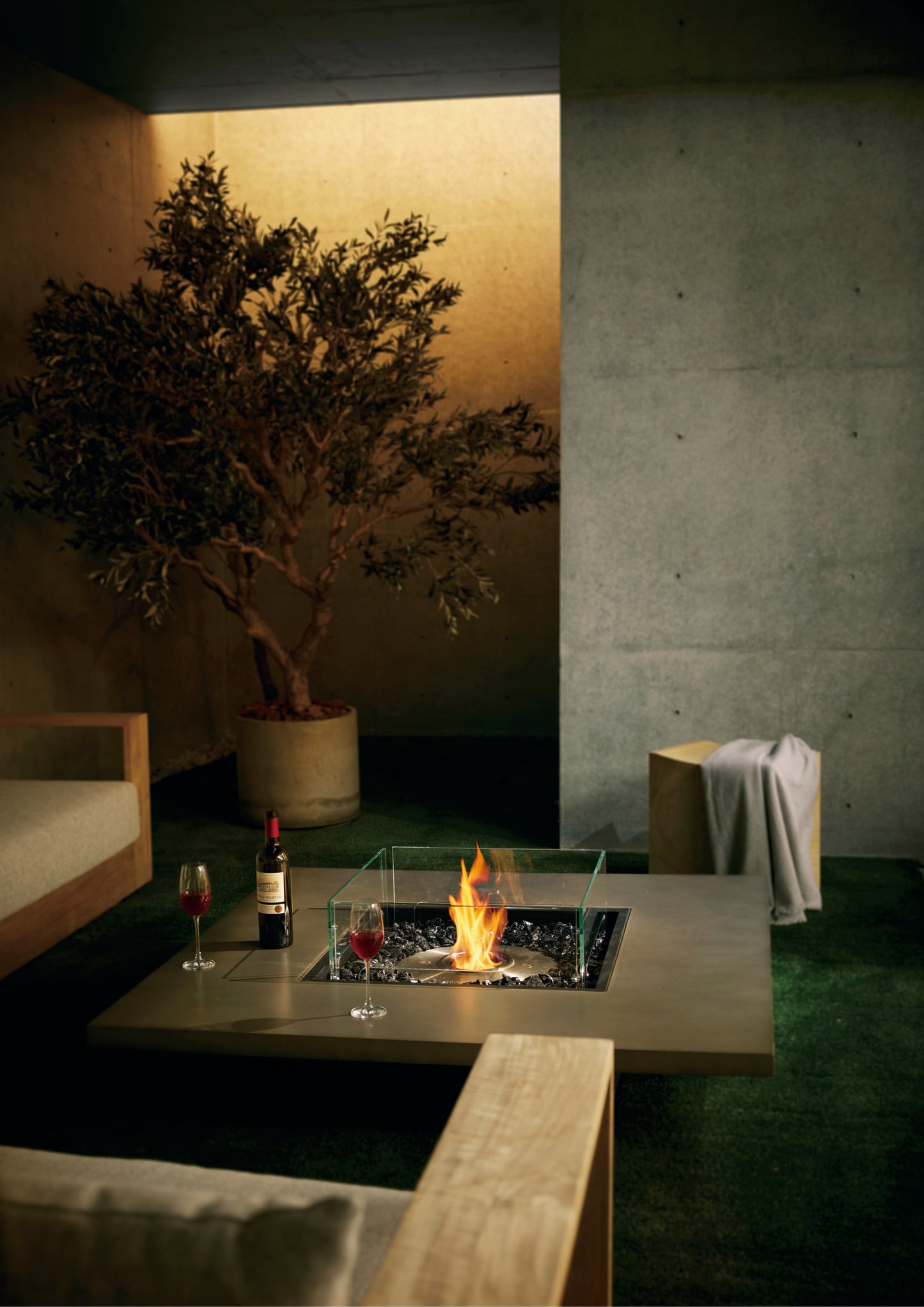 Modern outdoor setting with a fire pit, drinks, and a tree in a pot.