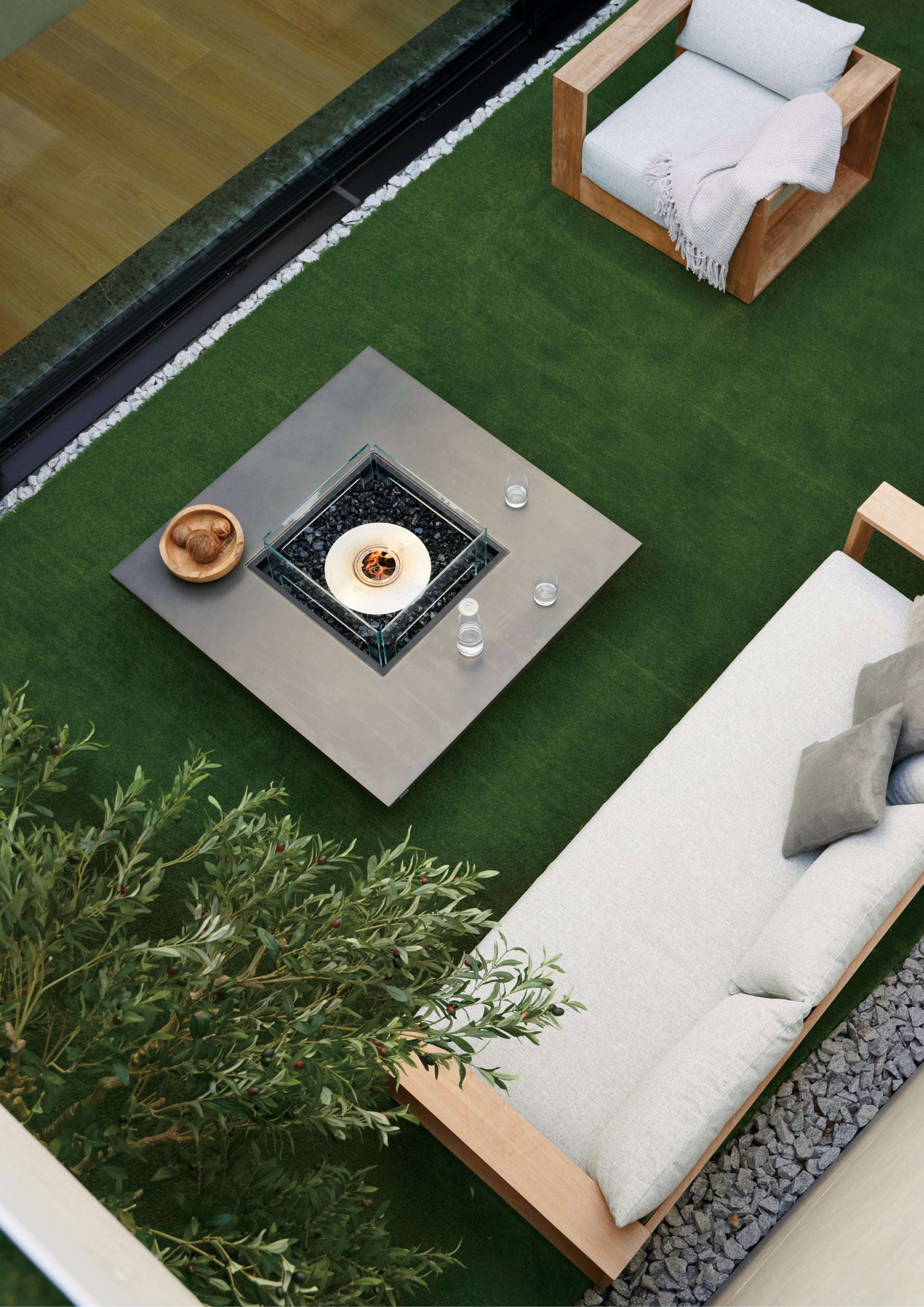 Outdoor patio with fire pit table, chairs, and a sofa on a green lawn.