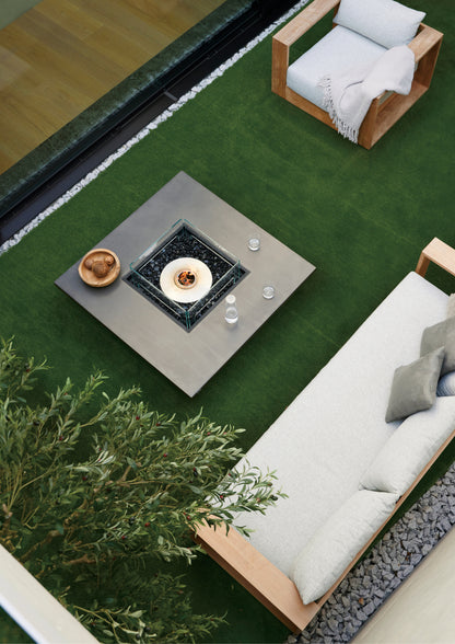 Outdoor patio with fire pit table, chairs, and a sofa on a green lawn.