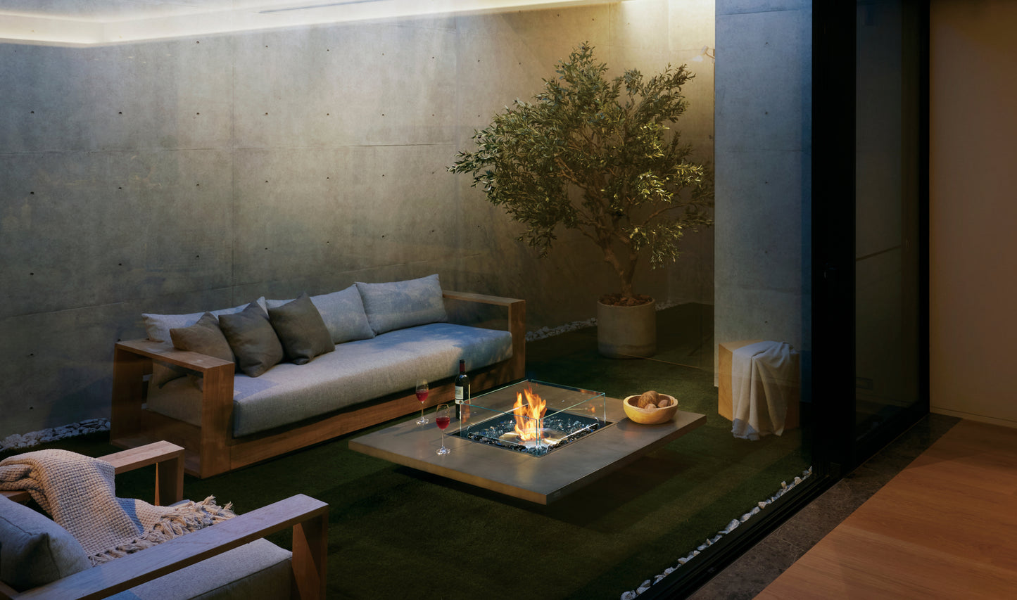 Modern outdoor living space with a fire pit, sofa, and potted plant.