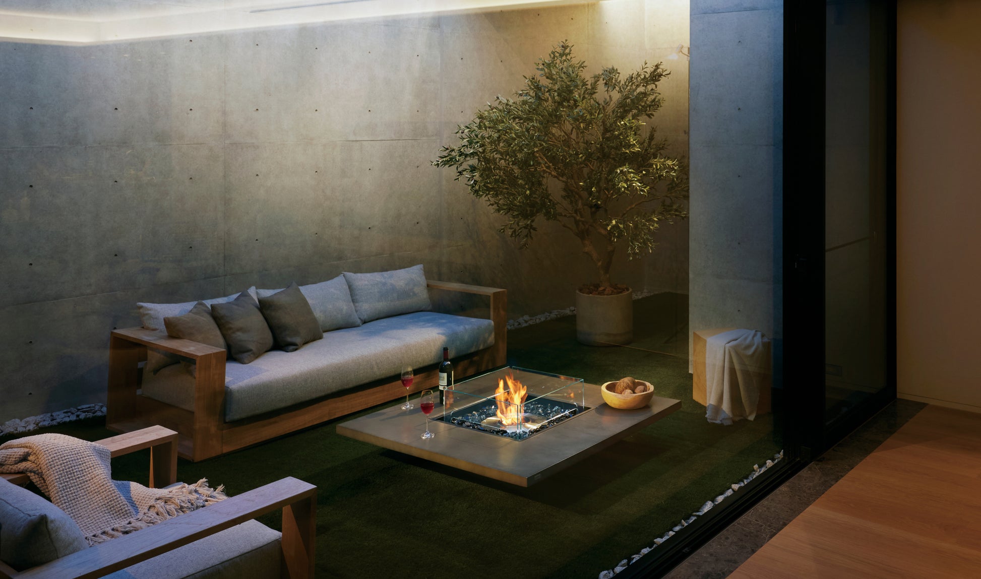 Modern outdoor living space with a fire pit, sofa, and potted plant.