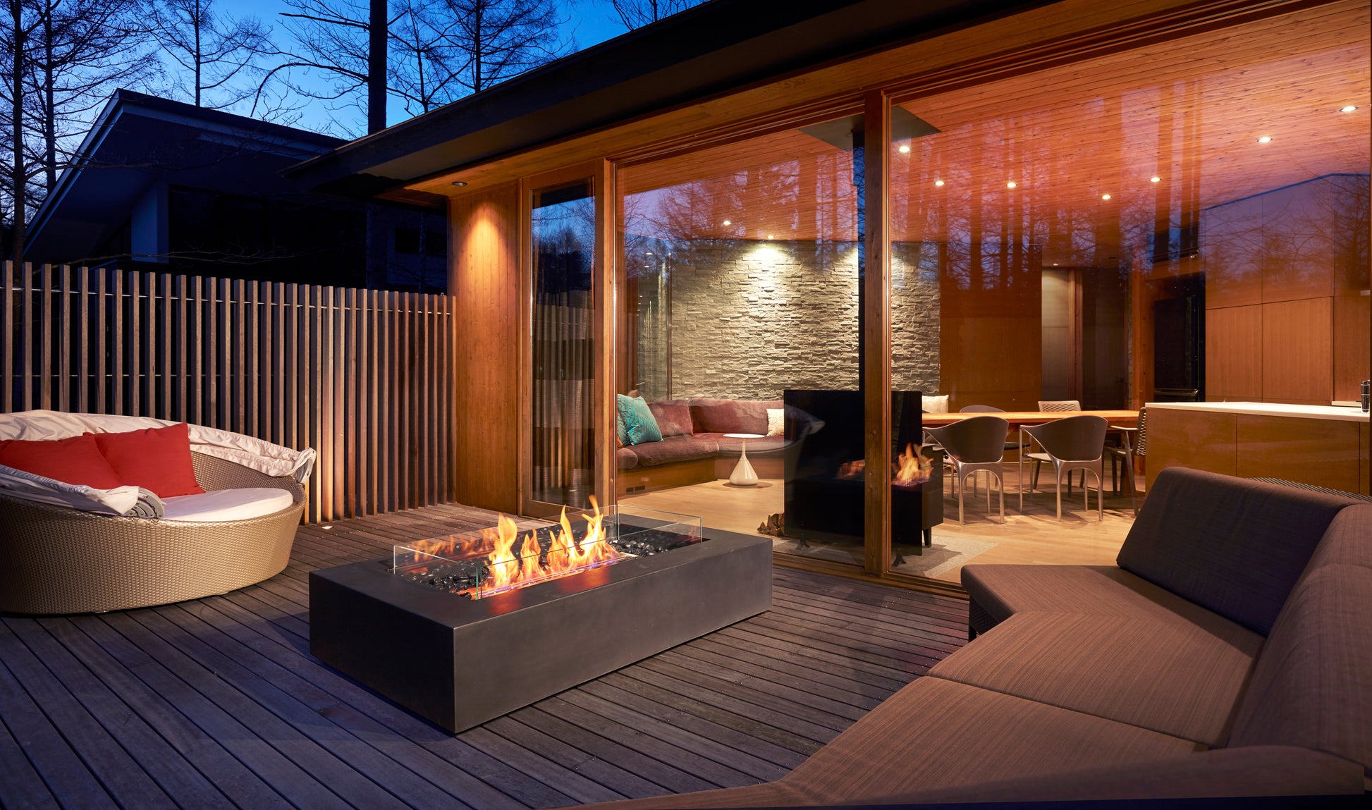 Modern outdoor living space with fire pit, seating area, and glass walls.