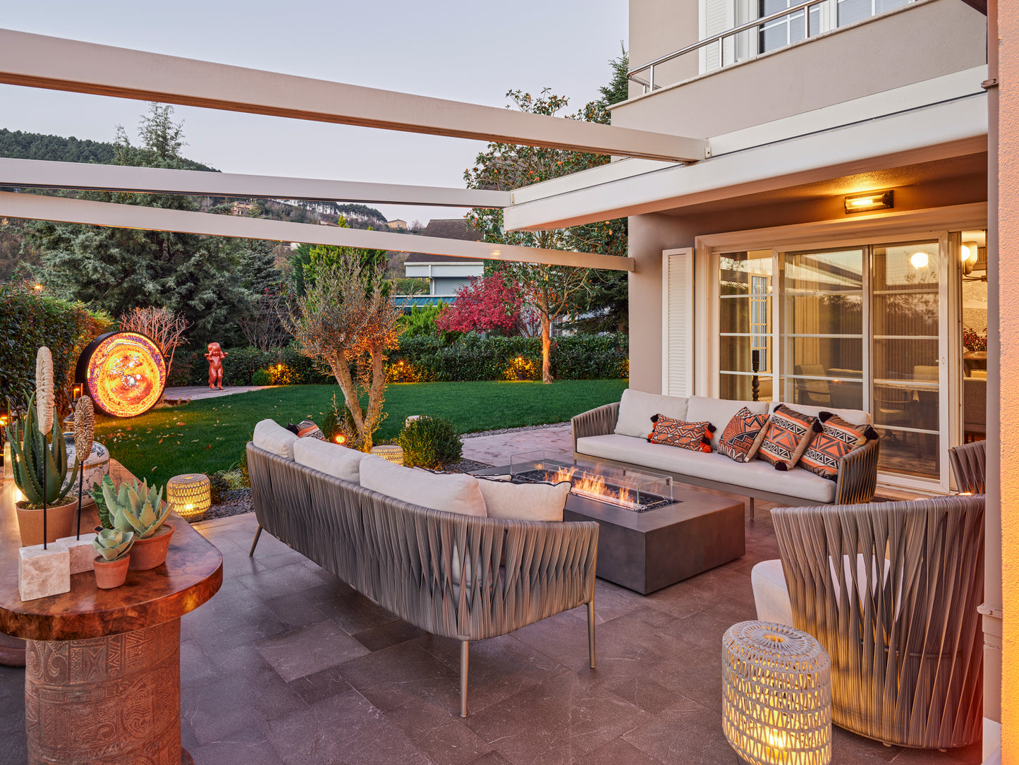 Outdoor patio area with furniture and lighting, featuring a modern house in the background.