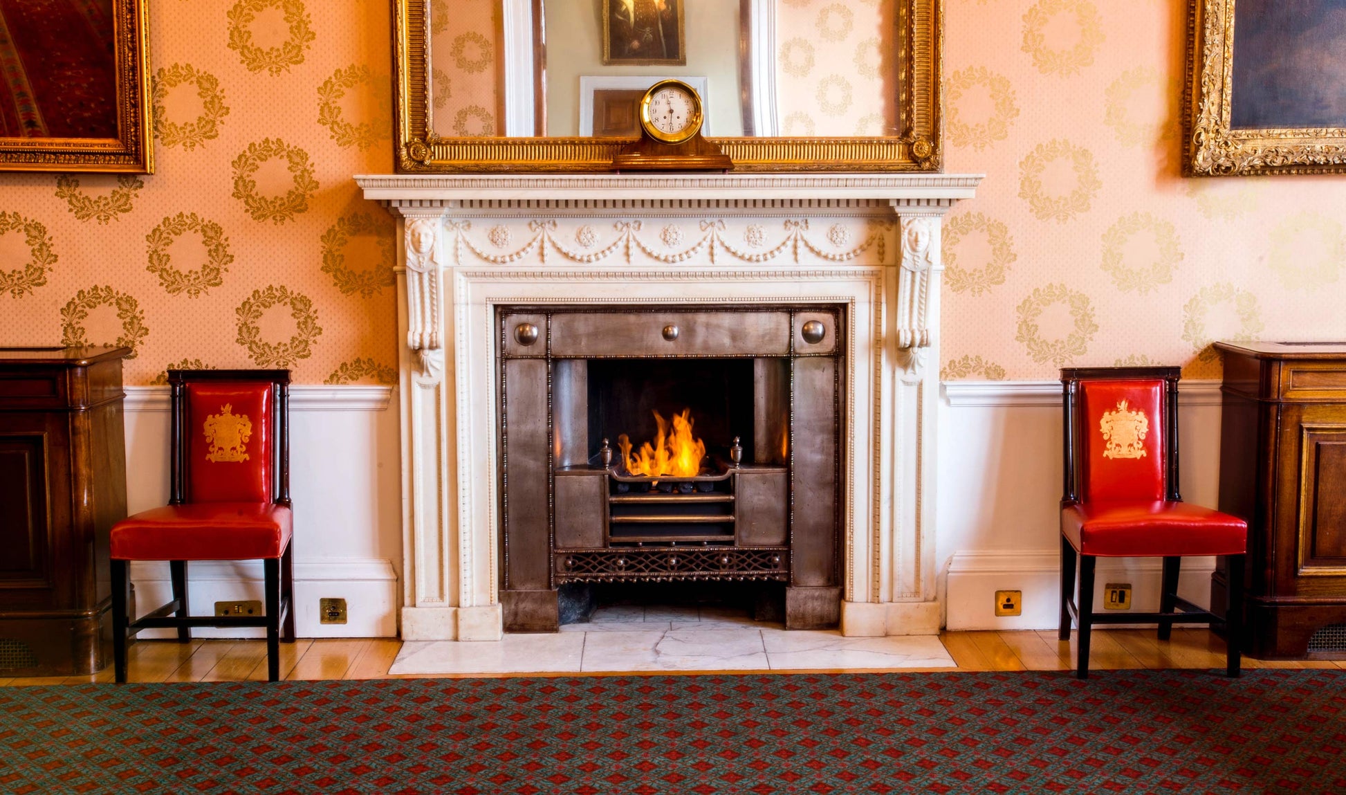 Fireplace with red chairs on either side in a room with decorative wallpaper.
