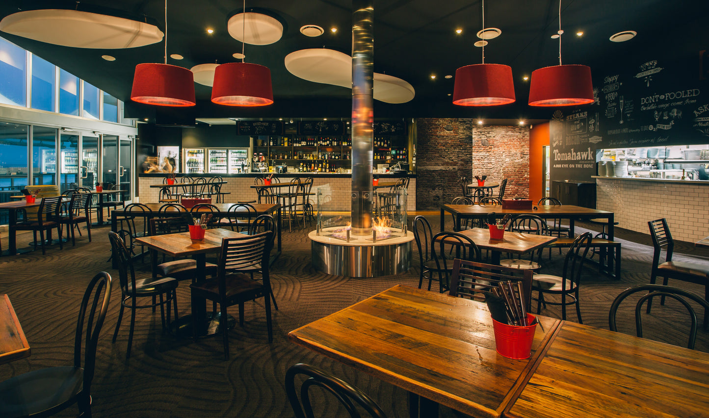 Modern restaurant interior with wooden tables, red chairs, and pendant lights.