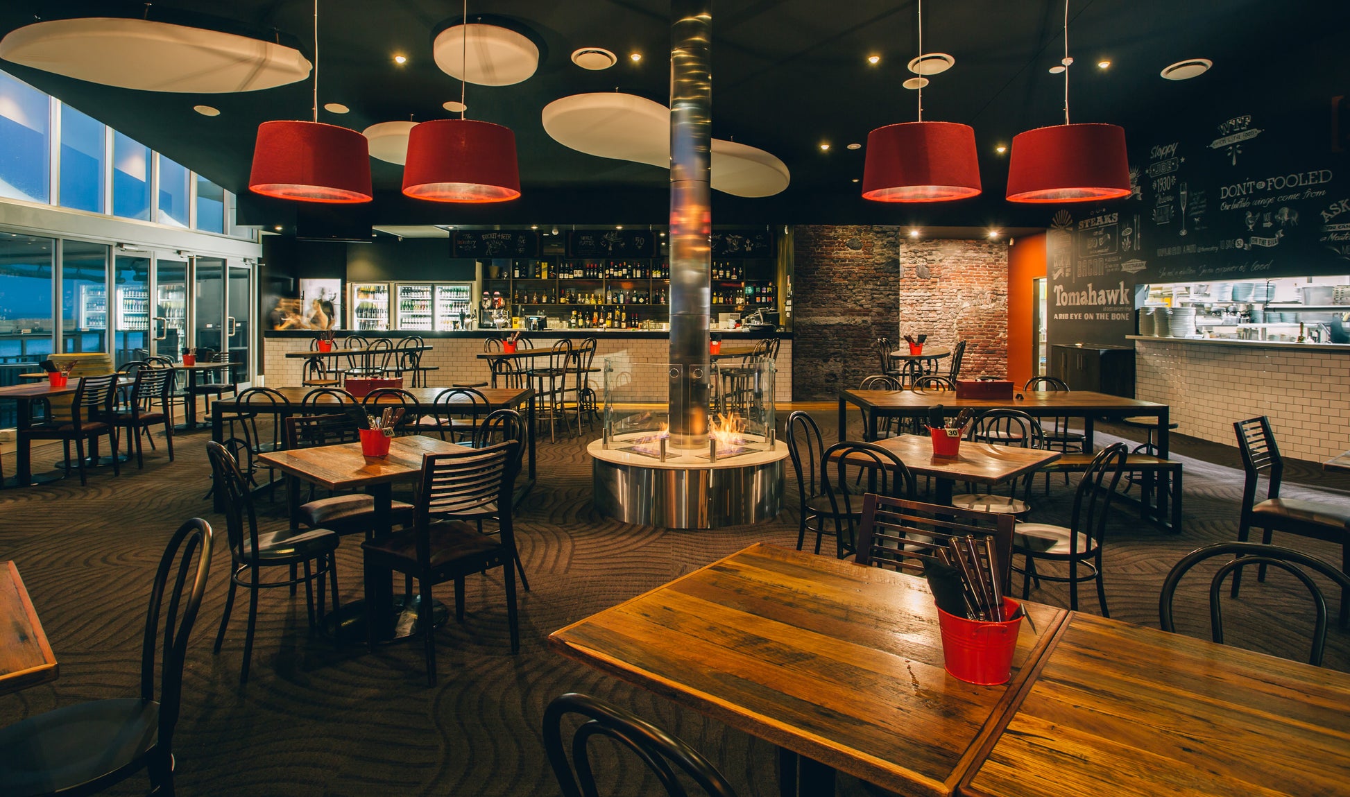 Modern restaurant interior with wooden tables, red chairs, and pendant lights.