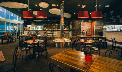 Modern restaurant interior with wooden tables, red chairs, and pendant lights.