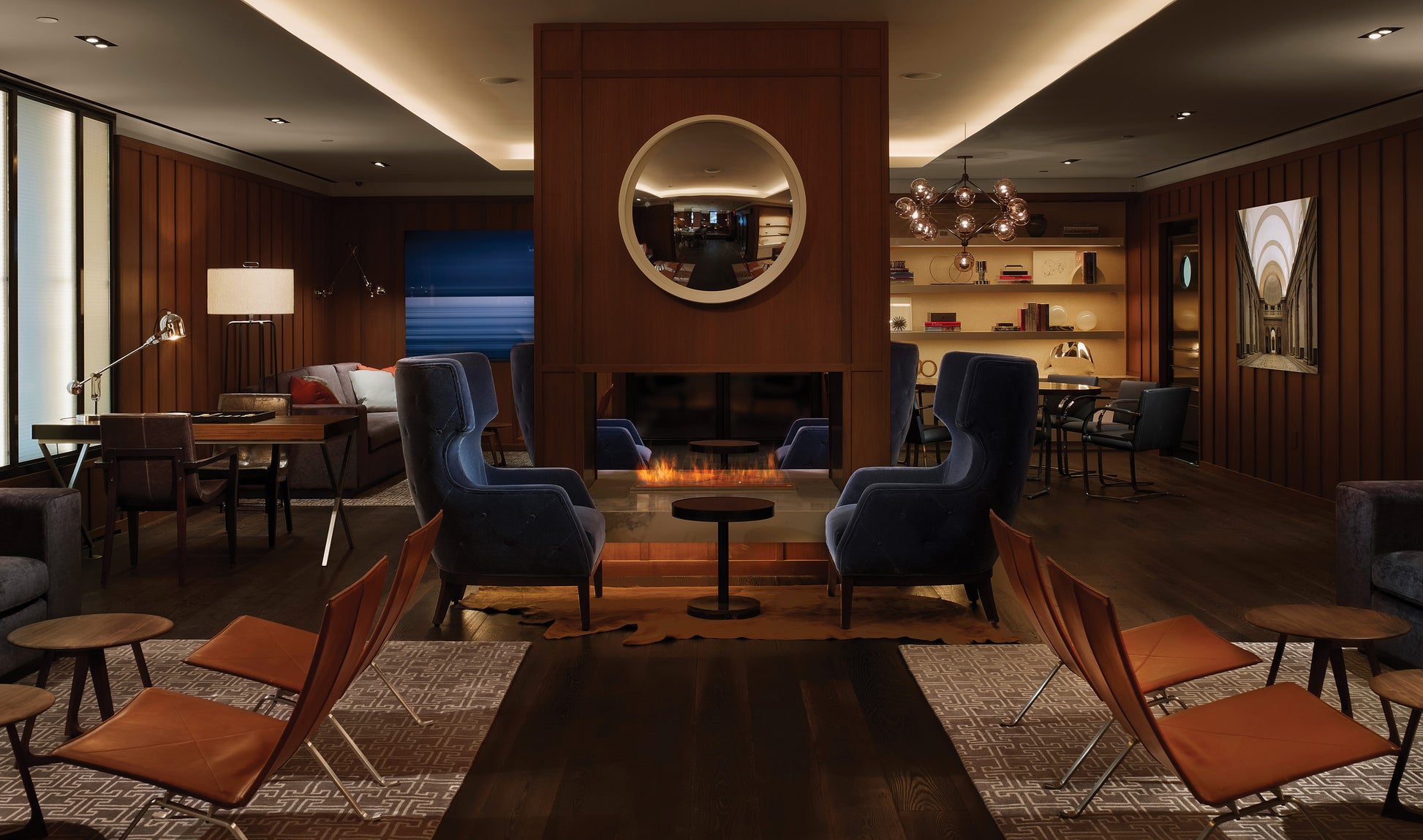 Modern lounge area with blue and orange chairs, a fireplace, and wooden walls.
