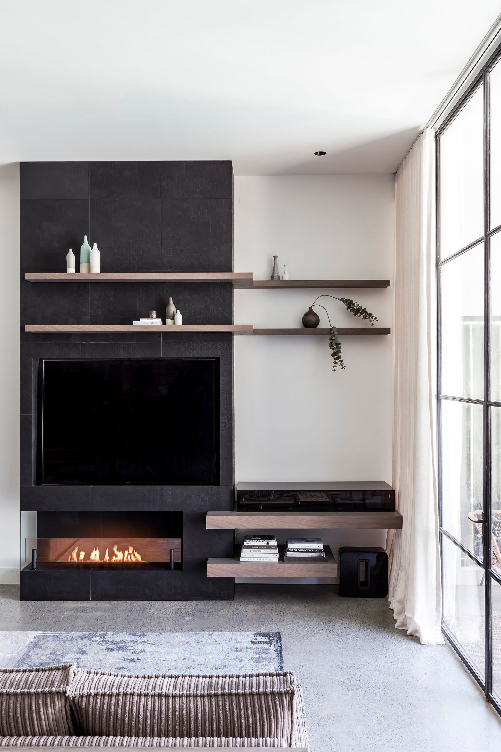 Modern living room with a black entertainment unit, TV, and shelves.
