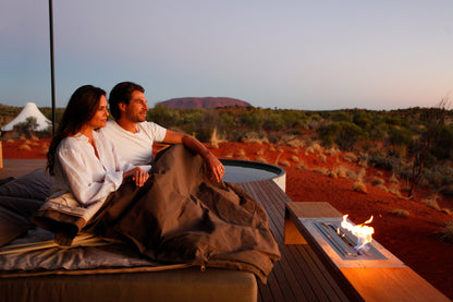 Couple sitting on a couch under a blanket overlooking a desert landscape with a fire pit.