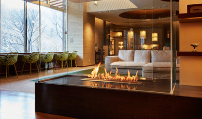Modern indoor setting with a fire pit, sofa, and chairs near large windows.
