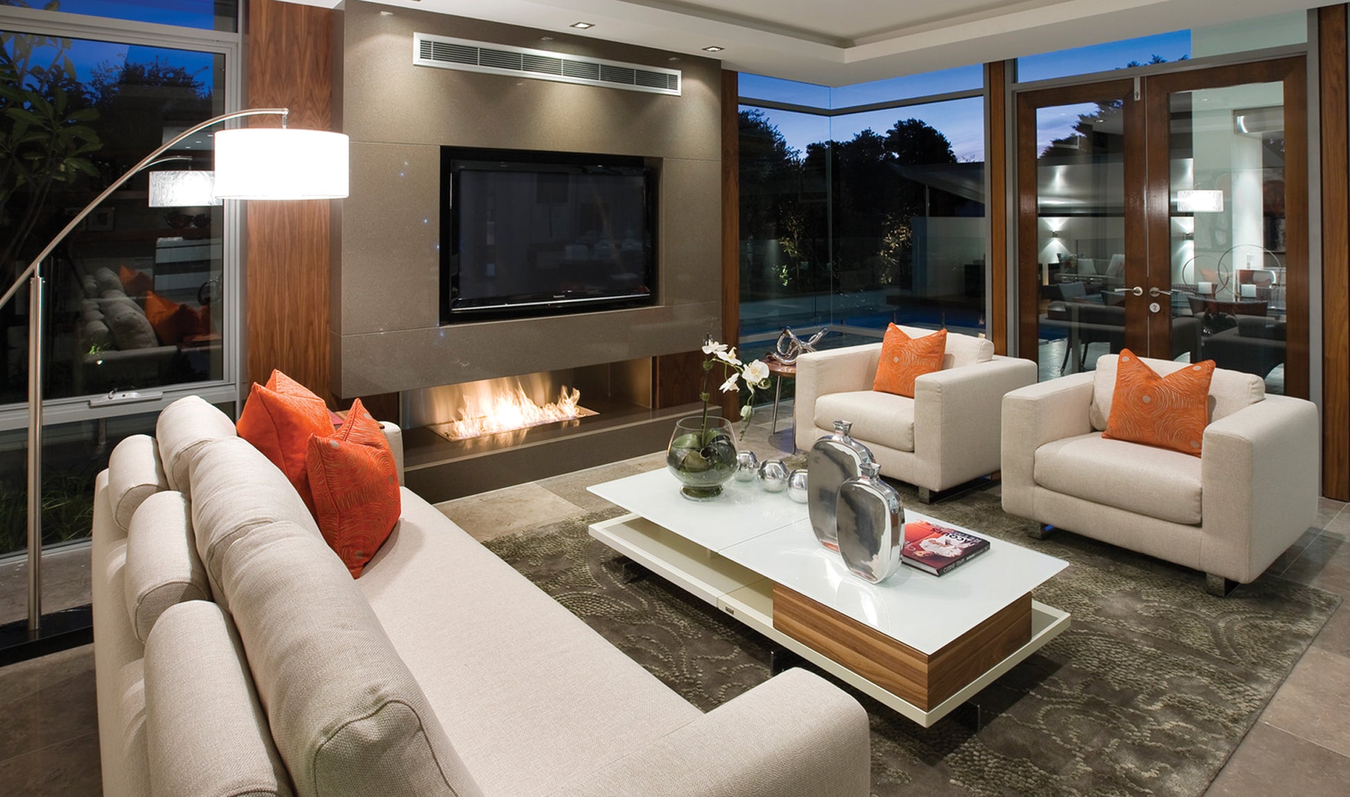 Modern living room with beige sofas, orange cushions, and a fireplace.