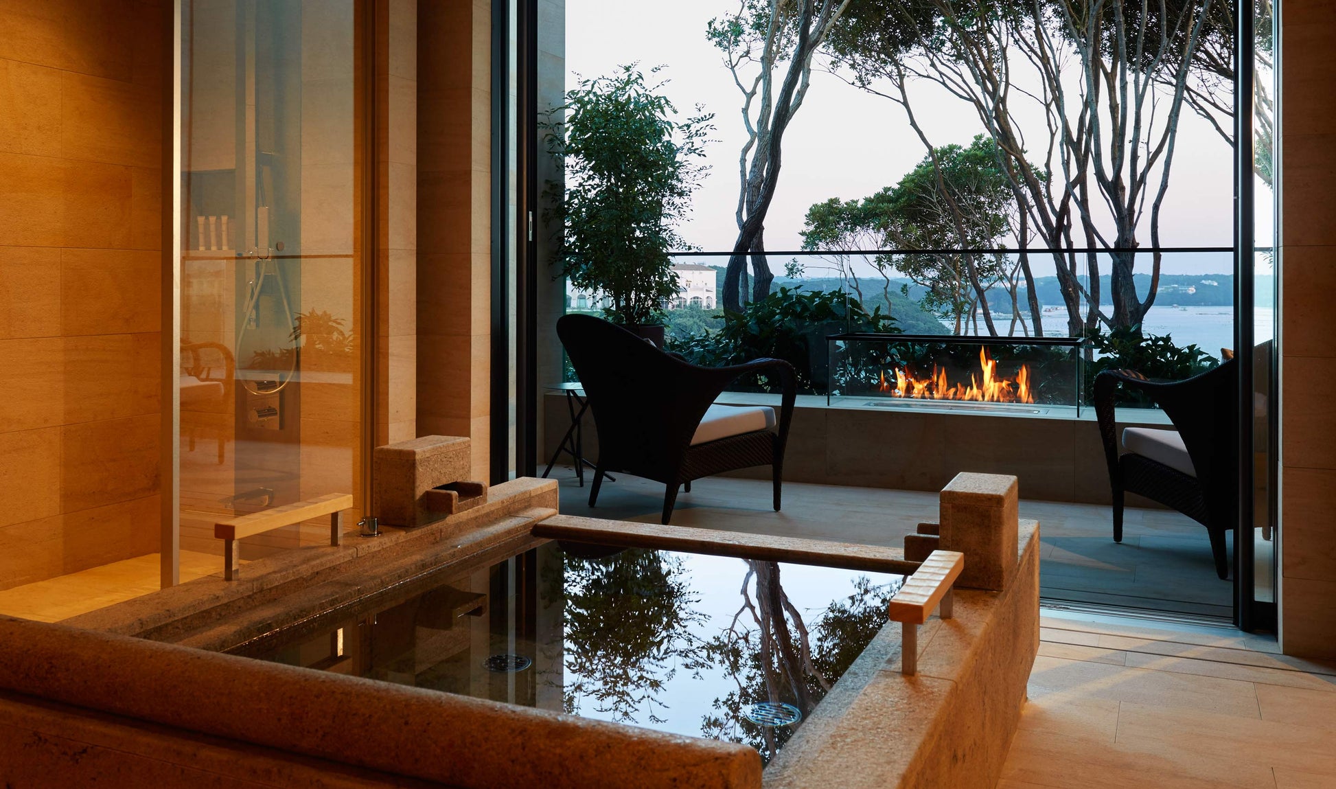 Modern indoor-outdoor living space with a fireplace and view of trees and water.