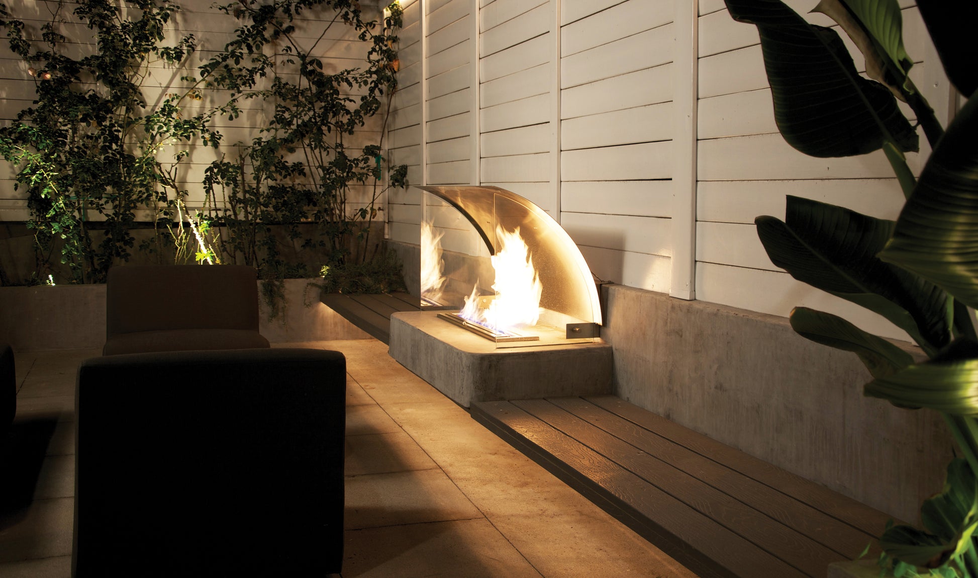 Modern outdoor setting with a fire pit, chairs, and plants.