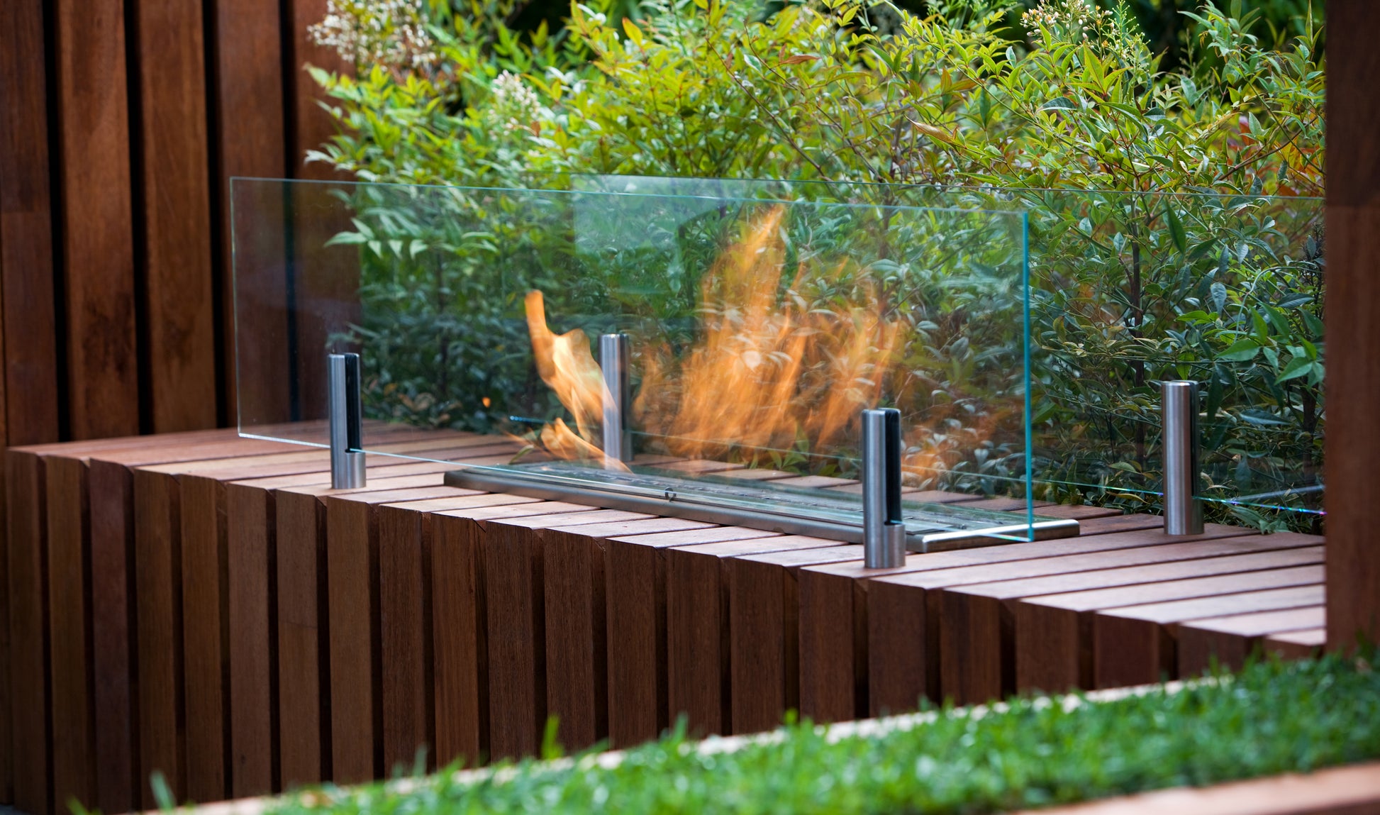 Outdoor fire pit with glass screen and wooden bench in a garden setting
