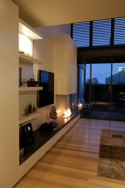 Modern living room with a television mounted on a wall, shelves with decorative items, and a large window view.
