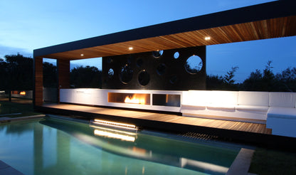Modern outdoor poolside area with a wooden canopy and fire pit at night.