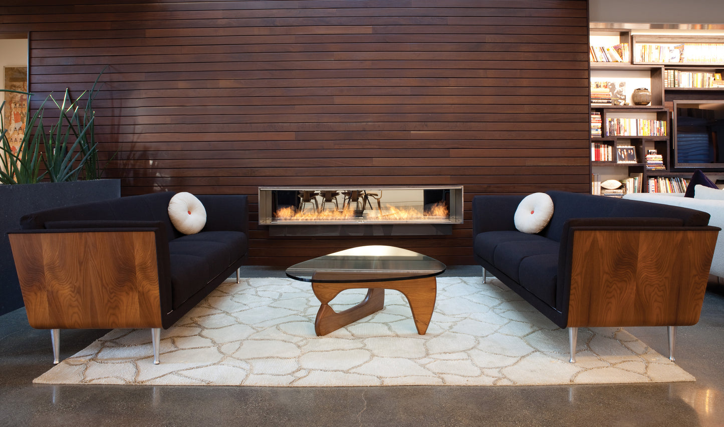 Modern living room with dark blue sofa, wooden coffee table, and bookshelf against a wooden wall.