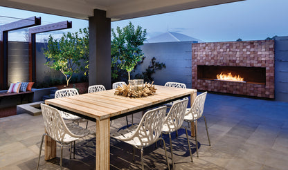 Outdoor dining area with wooden table and chairs near a fireplace.