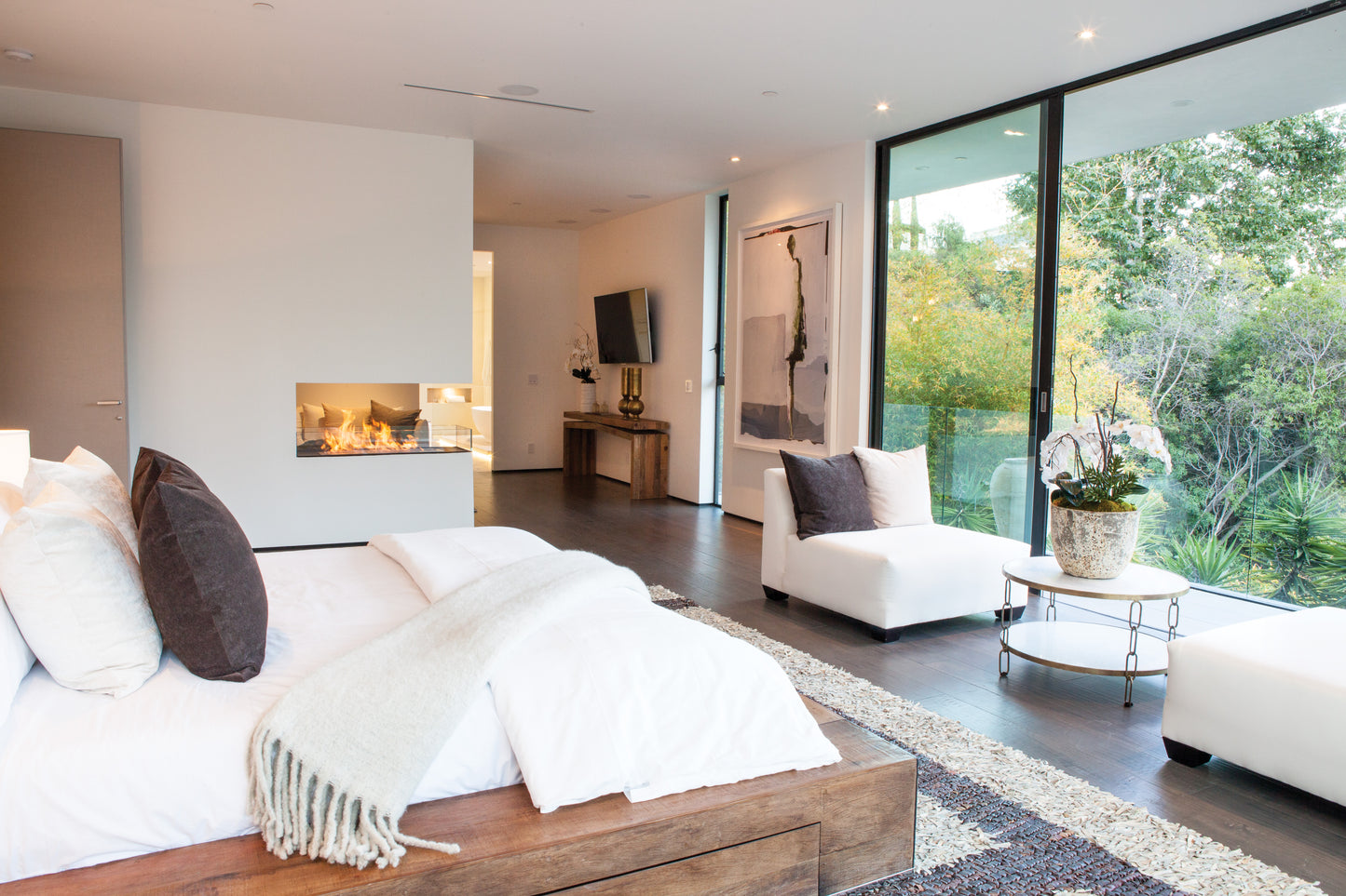 Modern bedroom with a bed, fireplace, and large windows.