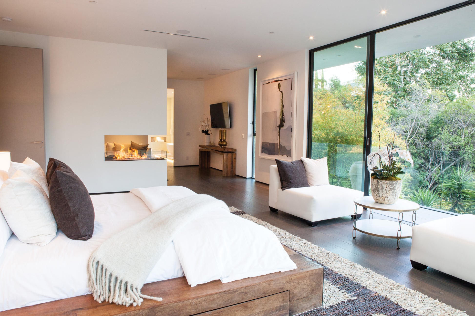 Modern bedroom with a bed, fireplace, and large windows.