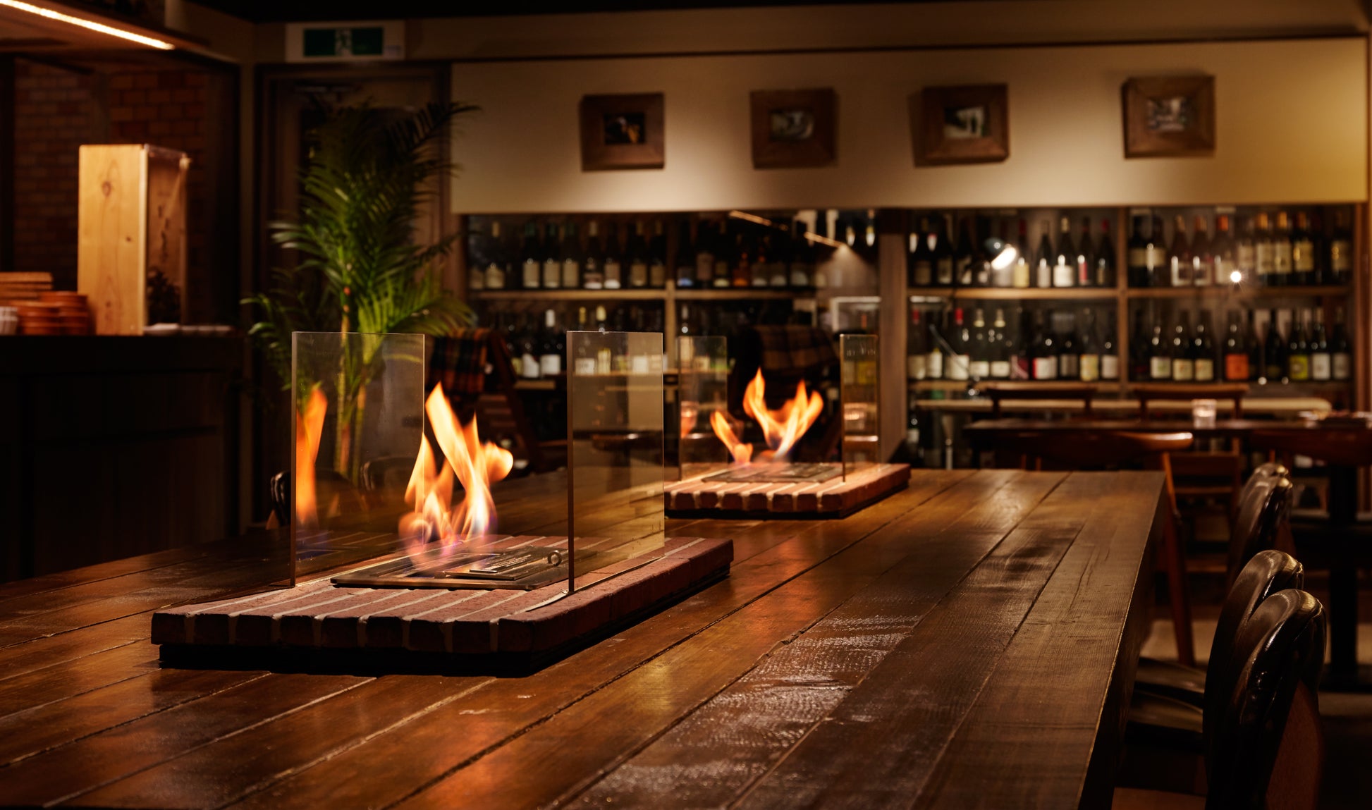 Two fire pits on a wooden table with a bar and wine bottles in the background