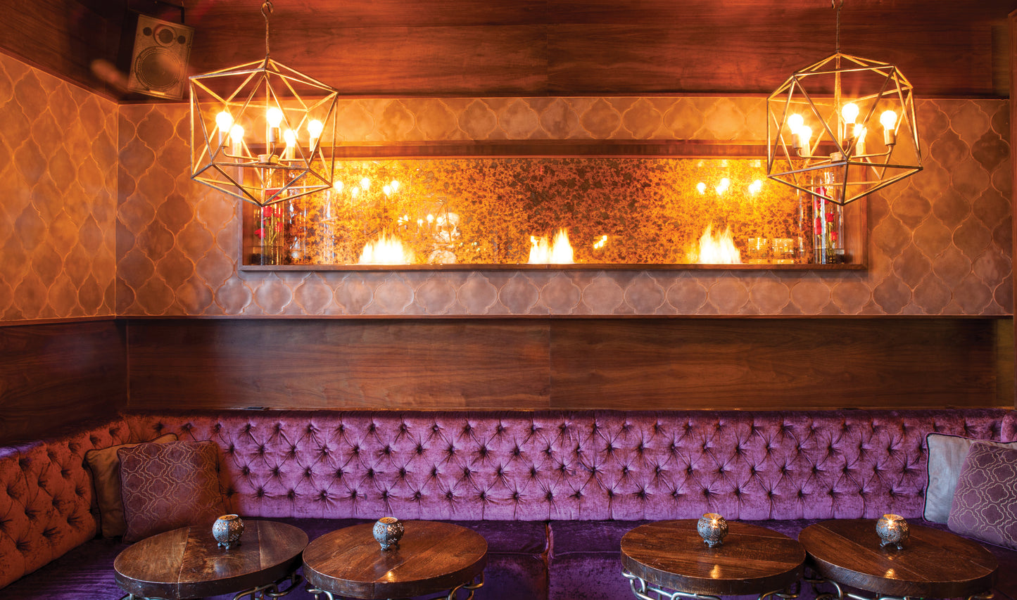 Decorative interior with purple velvet bench, wooden tables, and geometric light fixtures.
