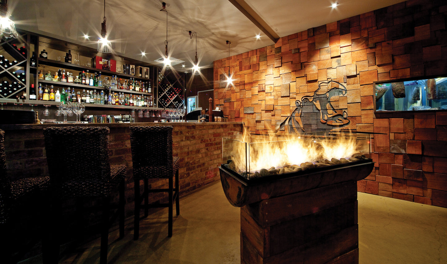 Bar area with wooden wall, fire pit, and bar stools.