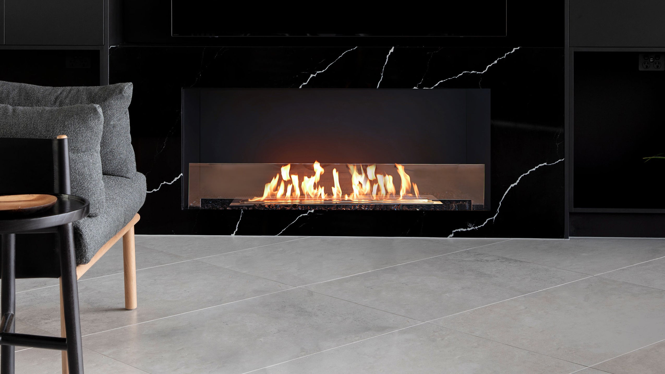 Modern bioethanol fireplace in marble setting, comfortable single seat lounge chair and side table on a tiled floor