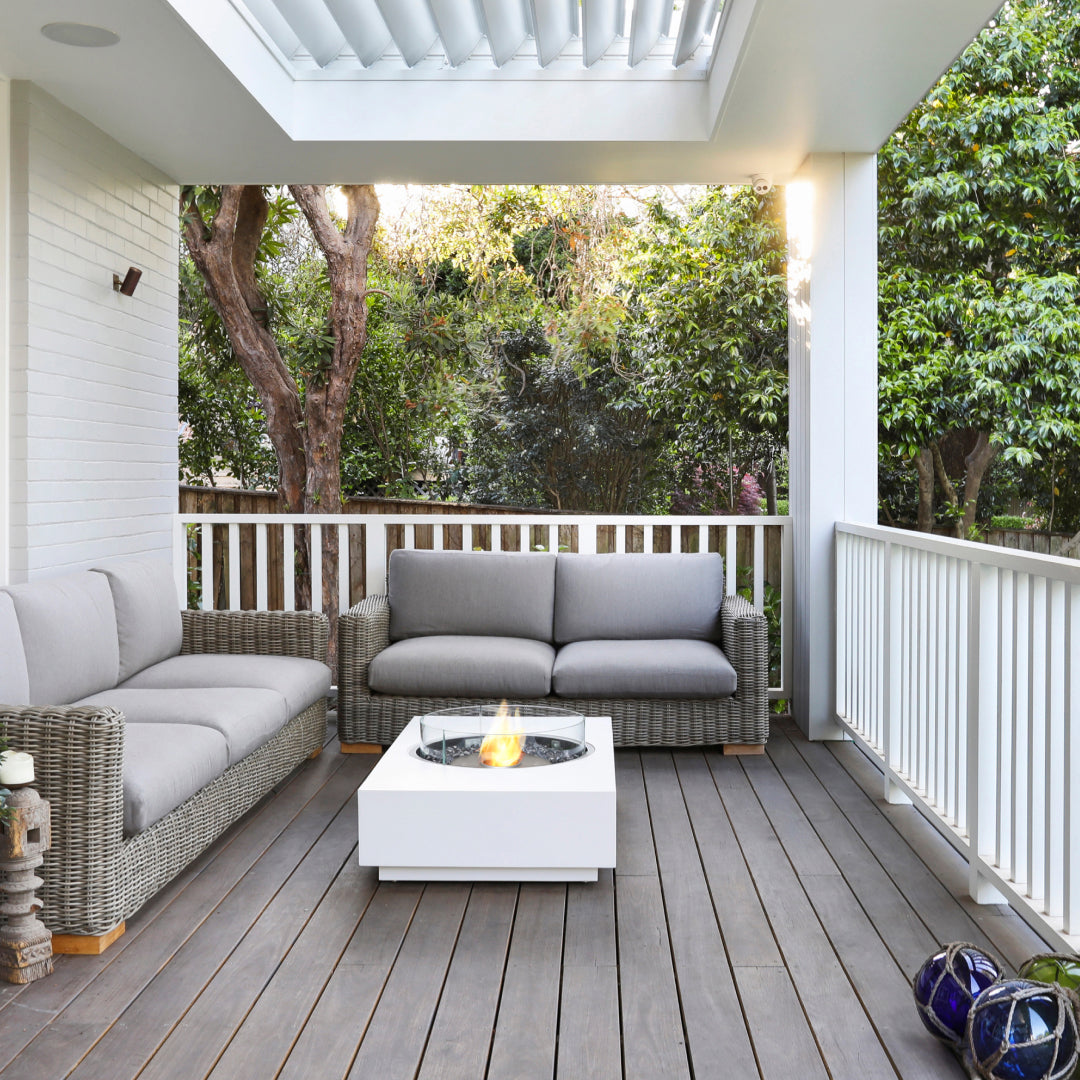 Outdoor patio with gray sofa, coffee table, and fire pit on a wooden deck.