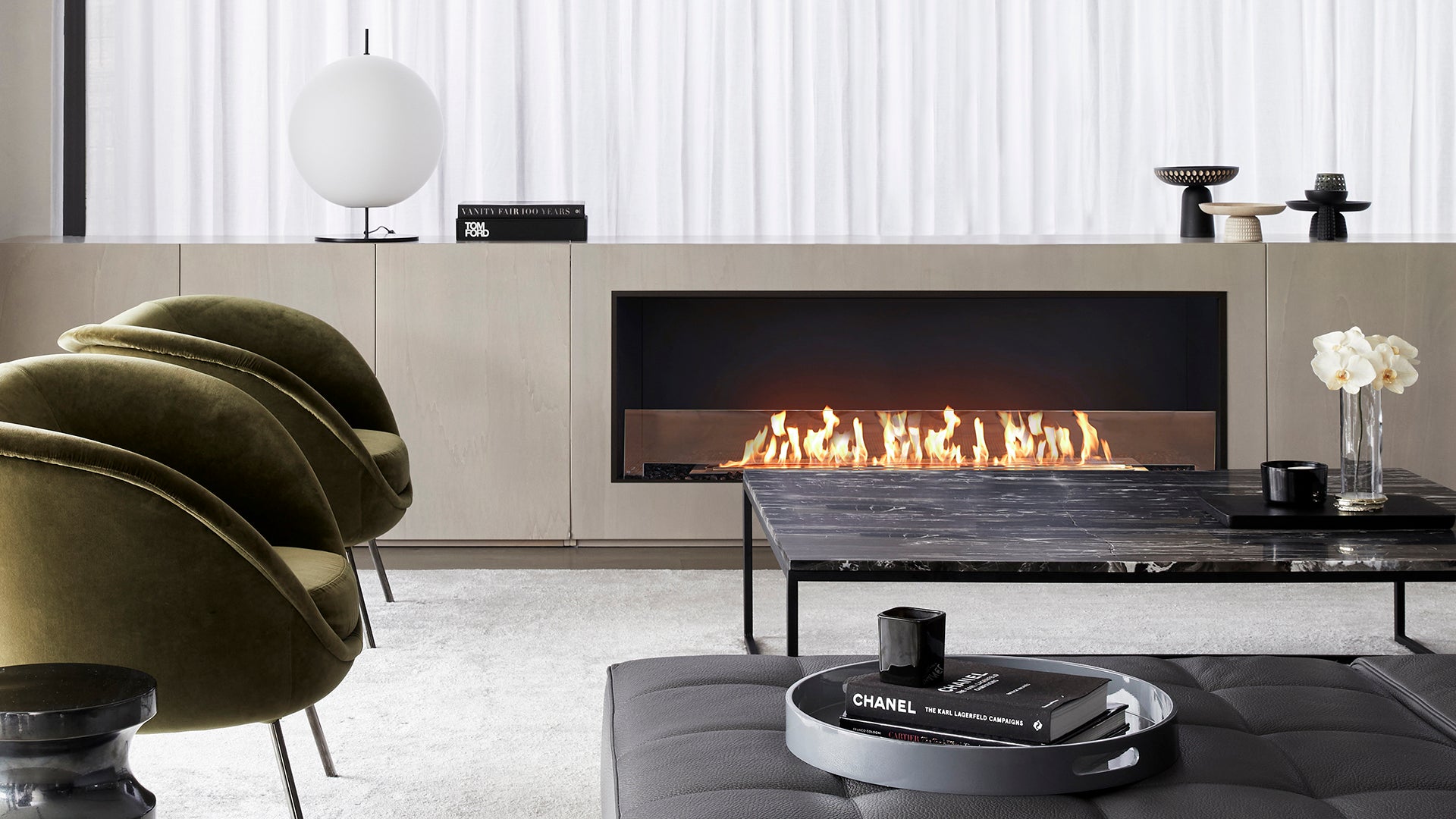 Modern living room with a fireplace, chairs, and a Chanel coffee table.