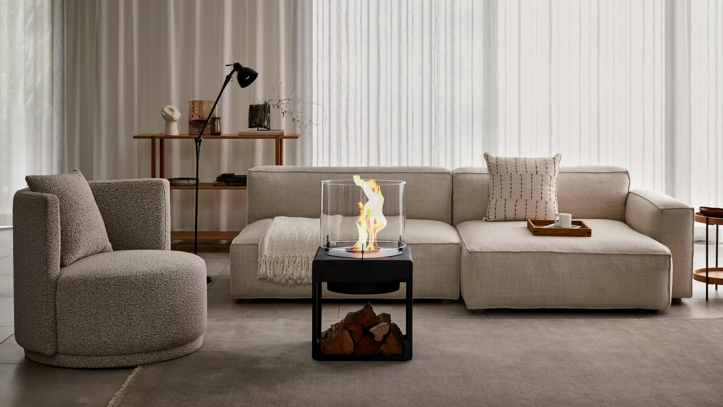 Modern living room with a beige sectional sofa, armchair, and a small table with a portable bioethanol fire pit.